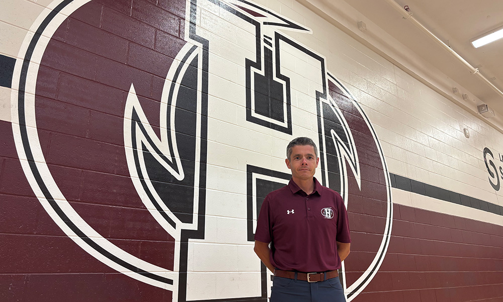 Adam Smith stands in front of the Holland Hurricanes Logo in the McMillan Centre for Community Engagement Gymnasium.